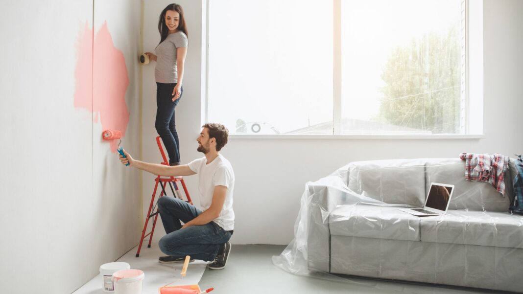 Young man and woman doing apartment repair together paint walls.