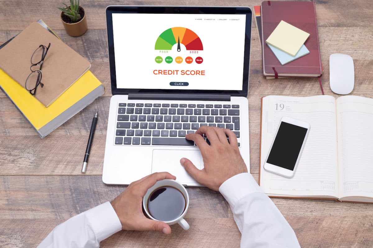 person's hands on computer reading credit score and holding cup of coffee on desk